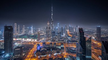 Panorama showing aerial view of tallest towers in Dubai Downtown skyline and highway night panorama. Financial district and business area in smart urban city. Skyscraper and high-rise buildings