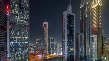 Panorama, Dubai Uluslararası Finans Bölgesi 'nin gökdelenler tarafından aydınlatılmış gece zaman çizelgesini gösteriyor. Çok katlı otoparkların yakınındaki bir yolda trafik vardı. Dubai, BAE.