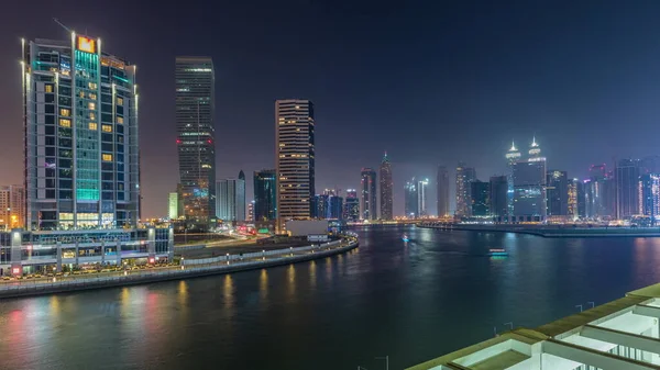 Modern city architecture in Business bay district at sunset. Panoramic aerial view of Dubai\'s skyscrapers reflected in water day to night transition timelapse