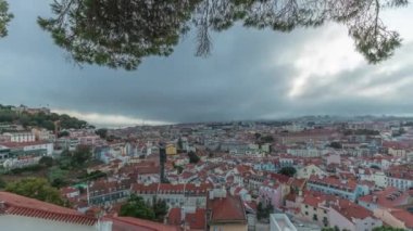 Panorama, gün batımından sonra Lizbon 'daki Miradouro da Graca' dan havadan şehre geçiş görüntülerini gösteriyor. Kırmızı çatılı ve akşam aydınlatmalı tarihi evlerin üzerinde dramatik bulutlar.