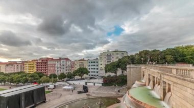 Panorama, Lizbon 'daki Jardim da Alameda' nın gün batımında Aydınlık Fonte Luminosa zaman dilimi ile hava görüntüsünü gösteriyor. Meydanı çevreleyen yeşil çimenli renkli evlerin üzerinde dramatik bulutlar
