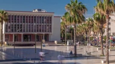 Arnavutluk 'un Durres kentindeki Sheshi Liria meydanındaki çeşme ve palmiye manzaralı tiyatro önünde yürüyüş sahası bulunuyor. Sokakta trafik vardı ve insanlar dolaşıyordu.