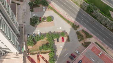 Dubai lüks konut bölgesinde hafif araçlar için araba park etmek, yukarıdan aşağıya doğru hava manzarası. Uzun gölgeli JLT gökdelenleri hızla hareket ediyor
