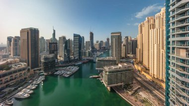 Güneş doğarken kanalın etrafındaki Dubai marina gökdelenlerine yüzen teknelerle hava panoramik görüntüsü. Yat kulübünde beyaz tekneler var.