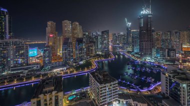 Panorama, Dubai Marina gökdelenlerini ve JBR bölgesini lüks binalar ve tatil köylerinin hava geceleriyle gösteriyor. Aydınlatılmış rıhtım ve kanalda yüzen tekneler