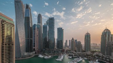 Dubai marina tallest skyscrapers and yachts in harbor aerial night to day transition during sunrise. View at apartment buildings, hotels and office blocks, modern residential development of UAE
