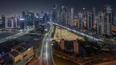 Panorama, Business Bay hava sahasında, Dubai, BAE 'de ışıklandırılmış modern kuleler inşa edildiğini gösteriyor. Büyük otoparkın yakınındaki yolda trafiği olan gökdelenler.