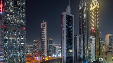 Panorama, Dubai Uluslararası Finans Bölgesi 'nin gökdelenlerle aydınlatılmış birçok gecesini gösteriyor. Çok katlı otoparkların yakınındaki bir yolda trafik vardı. Dubai, BAE.