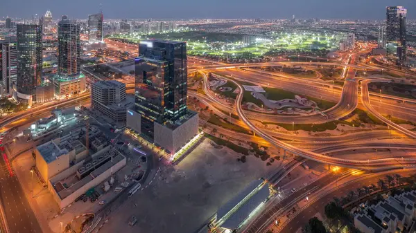 Huge highway crossroad junction between JLT district and media city intersected by Sheikh Zayed Road aerial day to night transition after sunset. Golf course near towers and skyscrapers with traffic