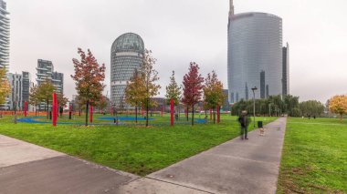 Panorama showing skyscrapers and biblioteca from park with green lawn and orange trees timelapse. Located between Piazza Gae Aulenti and Isola district. Traffic on a road intersection. Milan. Italy