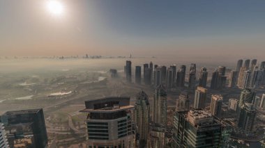 Dubai Marina Panoraması, güneş doğarken JLT gökdelenleri ve golf sahası, Dubai, Birleşik Arap Emirlikleri. Yukarıdan hava manzarası sisli bir sabah. Turuncu gökyüzü ile şehir silueti