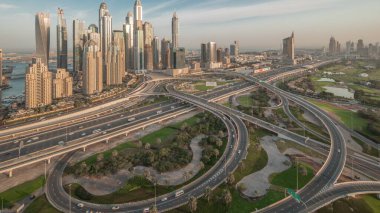 Dubai Marina karayolu kavşağı spagetti kavşağı panoraması. Arka planda en uzun gökdelenler ve golf sahası aydınlandı. Güneş doğmadan önce JLT bölgesinden hava üst görünümü