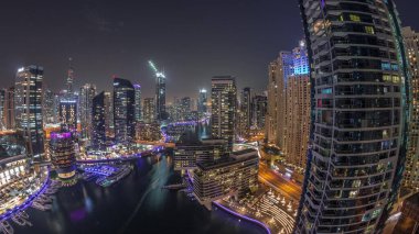 Kanal çevresindeki Dubai marina gökdelenleri ve gece gündüz yüzen tekneler. Günbatımından sonra beyaz tekneler yat kulübüne park edilir.