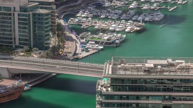 Kanal çevresindeki Dubai marina gökdelenlerinin yüzen tekneleriyle hava görüntüsü. Beyaz tekneler yat kulübüne park edilmiş. Sabah hareket eden gölgelerle dolu bir köprüde trafik vardı.