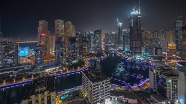 Panorama, Dubai Marina gökdelenlerini ve JBR bölgesini lüks binalar ve tatil köylerinin hava geceleriyle gösteriyor. Aydınlatılmış rıhtım ve kanalda yüzen tekneler
