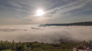 Panorama, Portekiz 'deki Sesimbra Town ve Port' un sisli zaman dilimi ile kaplı hava görüntüsünü gösteriyor. Bulutların tepesindeki manzara ve batan güneş. Setubal ilçesinde tatil köyü