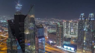 Dubai 'deki Sheikh Zayed Yolu' ndaki yüksek binalar gece uçuşları, BAE. Uluslararası finans bölgesinde yukarıdan aydınlatılmış gökdelenler. Arka planda evler ve villalar var.