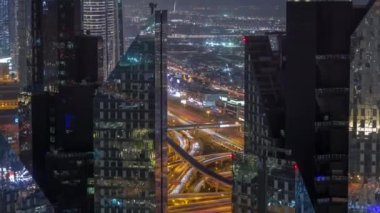 Dubai şehir merkezindeki gökdelenlerin arkasındaki yoğun yol kavşağına yukarıdan hava görüntüsü. Arabalar iki yöne de doğru ilerliyor. Aydınlatılmış kuleleri olan iş bölgesi