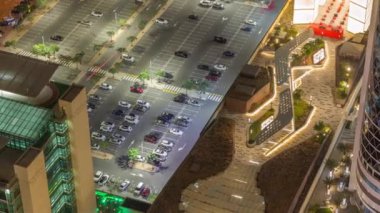 Otoparka park etmiş renkli arabaların hava manzarası. Park yerleri ve istikametler için çizgiler ve işaretler. Alışveriş caddesi yakınlarındaki Dubai finans bölgesi
