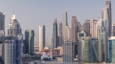 Dubai İşletme Koyu 'nun gökdelenleri ve su kanallarının zaman çizelgesi olan şehir manzarası. Rıhtımda konut ve ofis kuleleri olan modern gökyüzü. Yüksek binalarla çevrili bir cami.