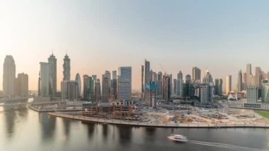 Dubai İşletme Koyu 'nun gökdelenleri ve su kanallarının zaman çizelgeleriyle gün batımı şehri. Rıhtımdaki konut ve ofis kulelerinin modern ufuk çizgisi. Peninsula 'da vinçleri olan büyük bir inşaat alanı.