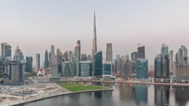 Hava panoramik görüntüsü Dubai Business Bay ve Downtown 'a kanal boyunca çeşitli gökdelenler ve kuleler ile gündüz ve gece geçiş zamanı. Gün batımından sonra vinçleri olan inşaat alanı