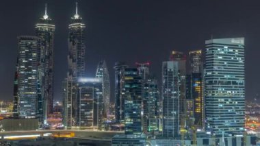 Dubai Business Bay 'in aydınlık gökdelenleri ve su kanalı hava gece zaman çizelgesine sahip şehir manzarası. Rıhtımdaki konut ve ofis kulelerinin modern ufuk çizgisi. Vinçler inşaat alanında çalışıyor
