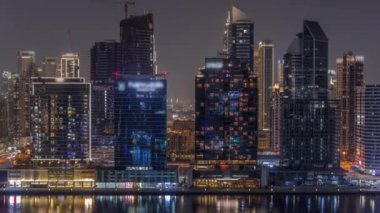 Dubai Business Bay ve şehir merkezinin havadan görüntüsü. Kanal gecesinde deniz kenarında parlayan pencereleri olan çeşitli gökdelenler ve kuleler. Vinçli inşaat alanı