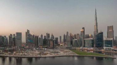 Dubai Business Bay ve Downtown 'ın havadan manzarası kanal boyunca çeşitli gökdelenler ve kuleler ile gündüz ve gece geçiş zamanı. Gün batımından sonra vinçleri olan inşaat alanı