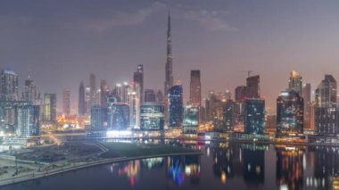 Dubai Business Bay ve Downtown 'ın havadan görüntüsü. Kanal boyunca çeşitli gökdelenler ve kuleler var. Gece gündüz geçiş zamanları. Güneş doğmadan önce vinçleri olan inşaat alanı
