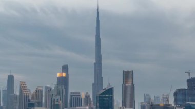 Dubai Business Bay ve Downtown 'ın havadan görüntüsü. Kanal boyunca çeşitli gökdelenler ve kuleler var. Gün ve gece geçiş zamanlarında. Gün batımından sonra vinçleri olan bir inşaat alanı. Bulutlu
