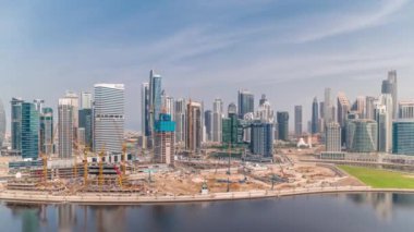 Dubai İş Körfezi 'nin gökdelenleri ve su kanalı hava zaman ayarlı şehir manzarası. Rıhtımda konut ve ofis kuleleri olan modern gökyüzü. Turnalar yeni bir bloğun şantiyesinde