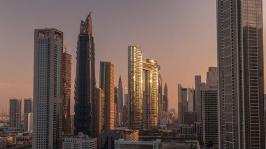 Dubai şehir merkezi ve finans bölgesinde caddelerde trafiği olan fütürist kuleler ve gökdelenler. Şehir silueti, gün doğumunda havadan sabah saatleri. Sıcak ışık ve güneş camdan yansıyor.
