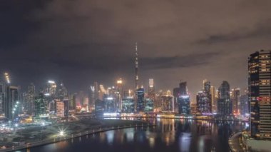 Dubai Business Bay ve Downtown 'a tüm gece boyunca sisle kaplı çeşitli gökdelenler ve kulelerle hava görüntüsü. Rıhtım ve kanal gece zaman çizelgesi. Vinçli inşaat alanı