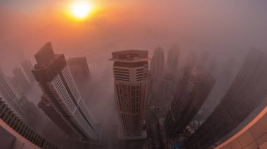 Dubai Marina ve JLT ufuk çizgisi üzerinde gün doğumunda nadir görülen kış sisi ve sokak ışıklarıyla aydınlatılan gökdelenler. Üst görünüm bulutların üstünde. Dubai, BAE