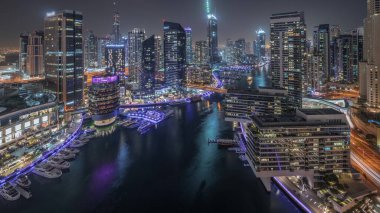 Panorama Dubai marinasının hava manzarasını gösteriyor. Kanal etrafındaki gökdelenleri aydınlatıyor. Yüzen yatlar ve gece saatleri var. Jlt ve JBR bölgelerindeki kuleler. Yat kulübünde beyaz tekneler var.