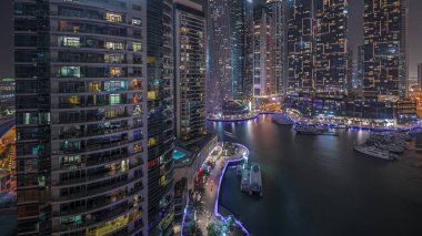 Panorama, Dubai marinasında gece hava sahasında lüks yat hangarını gösteriyor. Rıhtım boyunca modern gökdelenler ve limanda yüzen tekneler.