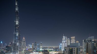 Panorama, Dubai şehir merkezinin aydınlatılmış mimarisiyle havadan çekilmiş gece zaman çizelgesini gösteriyor. Parlak pencereli birçok uzun gökdelen ve kuleler. Yeni inşaat alanı.