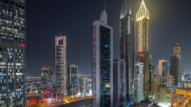 Panorama, Dubai Uluslararası Finans Bölgesi 'nin gökdelenler tarafından aydınlatılmış gece zaman çizelgesini gösteriyor. Çok katlı otoparkların yakınındaki bir yolda trafik vardı. Dubai, BAE.
