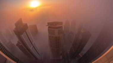 Dubai Marina ve JLT ufuk çizgisi üzerinde gün doğumunda nadir görülen kış sisi ve sokak ışıklarıyla aydınlatılan gökdelenler. Üst görünüm bulutların üstünde. Dubai, BAE
