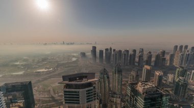Dubai Marina Panoraması 'nda güneş doğarken JLT gökdelenleri ve golf sahası, Dubai, Birleşik Arap Emirlikleri. Yukarıdan hava manzarası sisli bir sabah. Turuncu gökyüzü ile şehir silueti