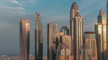 Dubai Marina 'nın gökdelenleri gece gündüz geçiş zamanlarında en yüksek konut binalarıyla aydınlandı. JLT bölgesinden hava görüntüsü. Güneş doğarken camdan yansıyor.