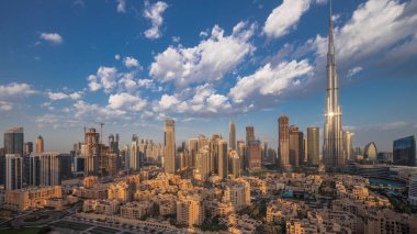 Dubai Downtown night to day transition with reflections on tallest skyscraper and other towers view from the top during sunrise, United Arab Emirates. Traditional houses of old town and pink clouds