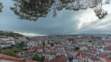 Panorama, gün batımından sonra Lizbon 'daki Miradouro da Graca' dan havadan şehre geçiş görüntülerini gösteriyor. Kırmızı çatılı ve akşam aydınlatmalı tarihi evlerin üzerinde dramatik bulutlar.