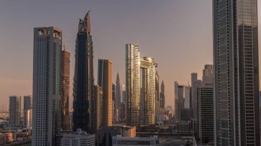 Dubai şehir merkezi ve finans bölgesinde caddelerde trafiği olan fütürist kuleler ve gökdelenler. Şehir silueti, gün doğumunda havadan sabah saatleri. Sıcak ışık ve güneş camdan yansıyor.