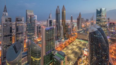 Sheikh Zayed Yolu 'ndaki yüksek binaların gökyüzü manzarası gece gündüz Dubai hava geçiş zamanı, BAE. Uluslararası Finans Merkezi 'ndeki gökdelenler güneş doğarken uzun gölgelerle tepeden görünüyor.