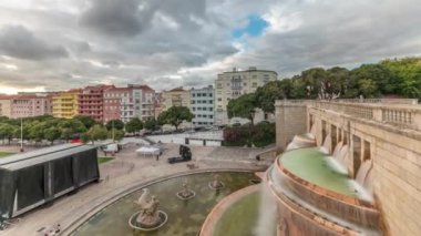 Panorama, Lizbon 'daki Jardim da Alameda' nın gün batımında Aydınlık Fonte Luminosa zaman dilimi ile hava görüntüsünü gösteriyor. Meydanı çevreleyen yeşil çimenli renkli evlerin üzerinde dramatik bulutlar
