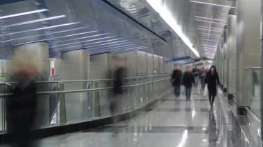 Nakil koridoru zaman ayarlı modern bir metro istasyonu. İstasyonlar arasında yürüyen insanlar. Yerde yansımalar var.