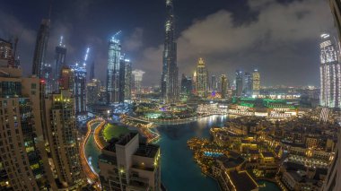 Dubai 'de gökdelenler gün be gece yükseliyor geçiş zamanı, alışveriş merkezi ve çeşme modern binalarla çevrili havadan panoramik manzara bulutlu gün batımı gökyüzü