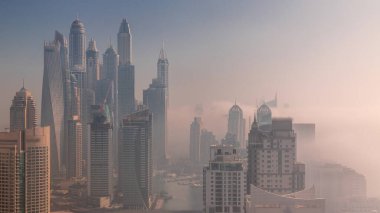 Sunrise Airial Timelapse sırasında Dubai Marina 'nın en yüksek konut bloğundaki yapay kanallı çeşitli gökdelenlerin görüntüsü. Birçok kule ve yat sabah sisi ile kaplandı.